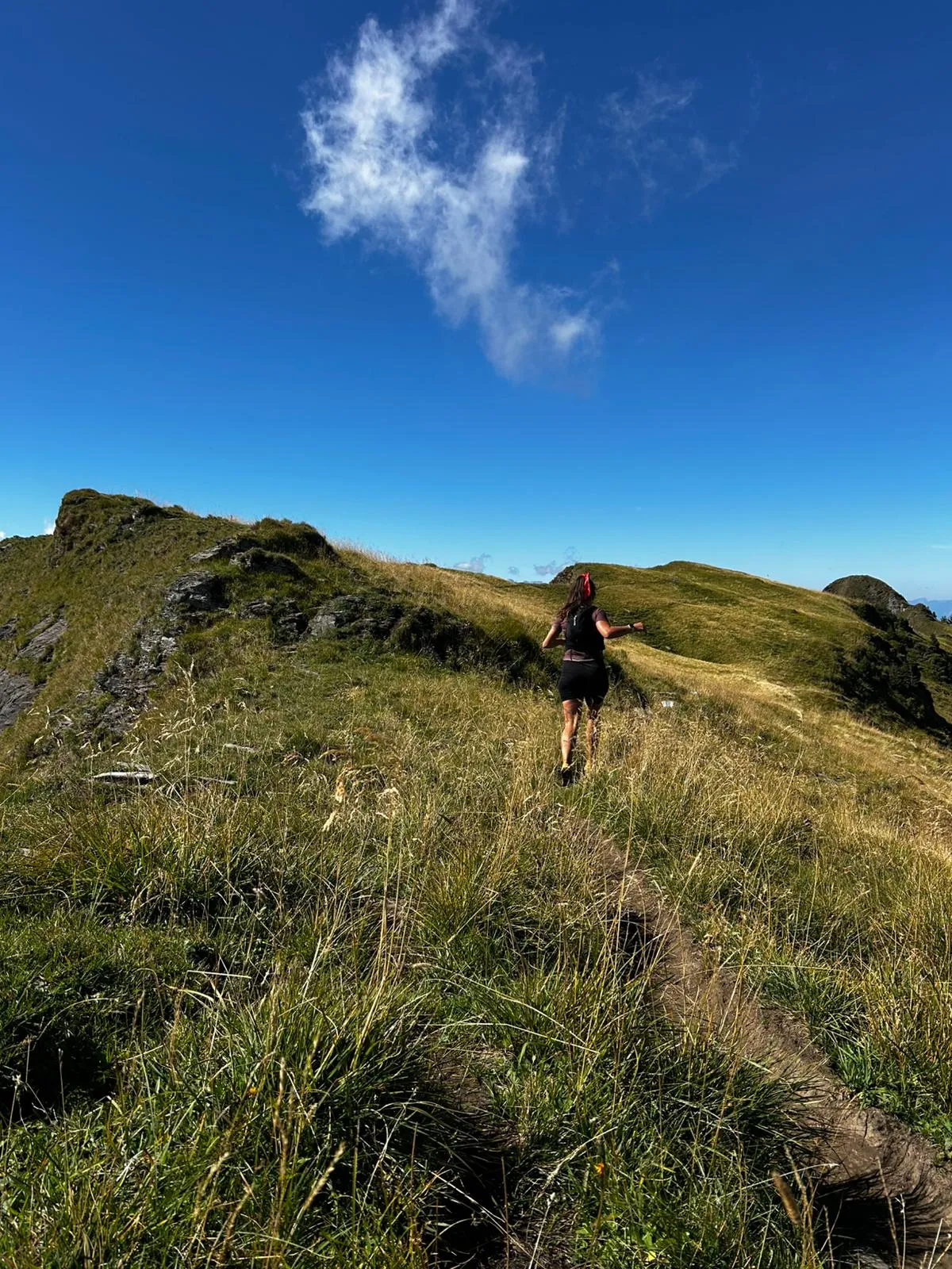 A runner in a red headband runs up the grassy crest of the ridge, a single wisp of cloud in the deep blue sky above.