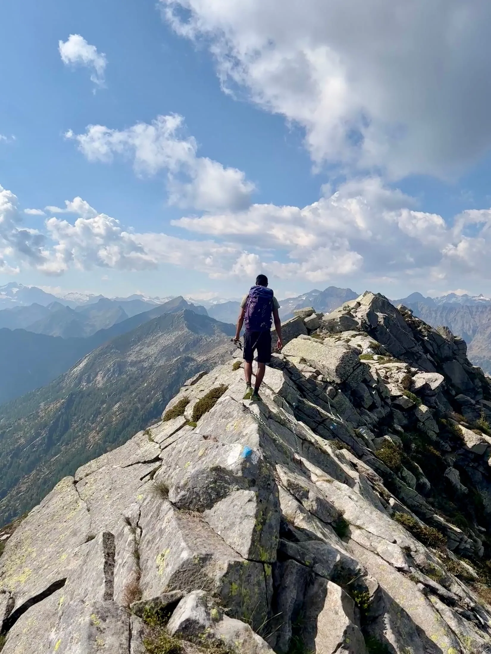 A hiker walks along a broad granite summit ridge with peaks spread out in every direction.