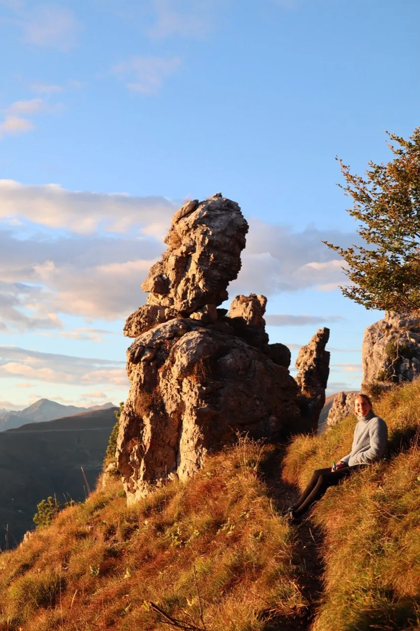 Hiker relaxing beside a jagged rock tooth of the Denti della Vecchia in golden evening light.