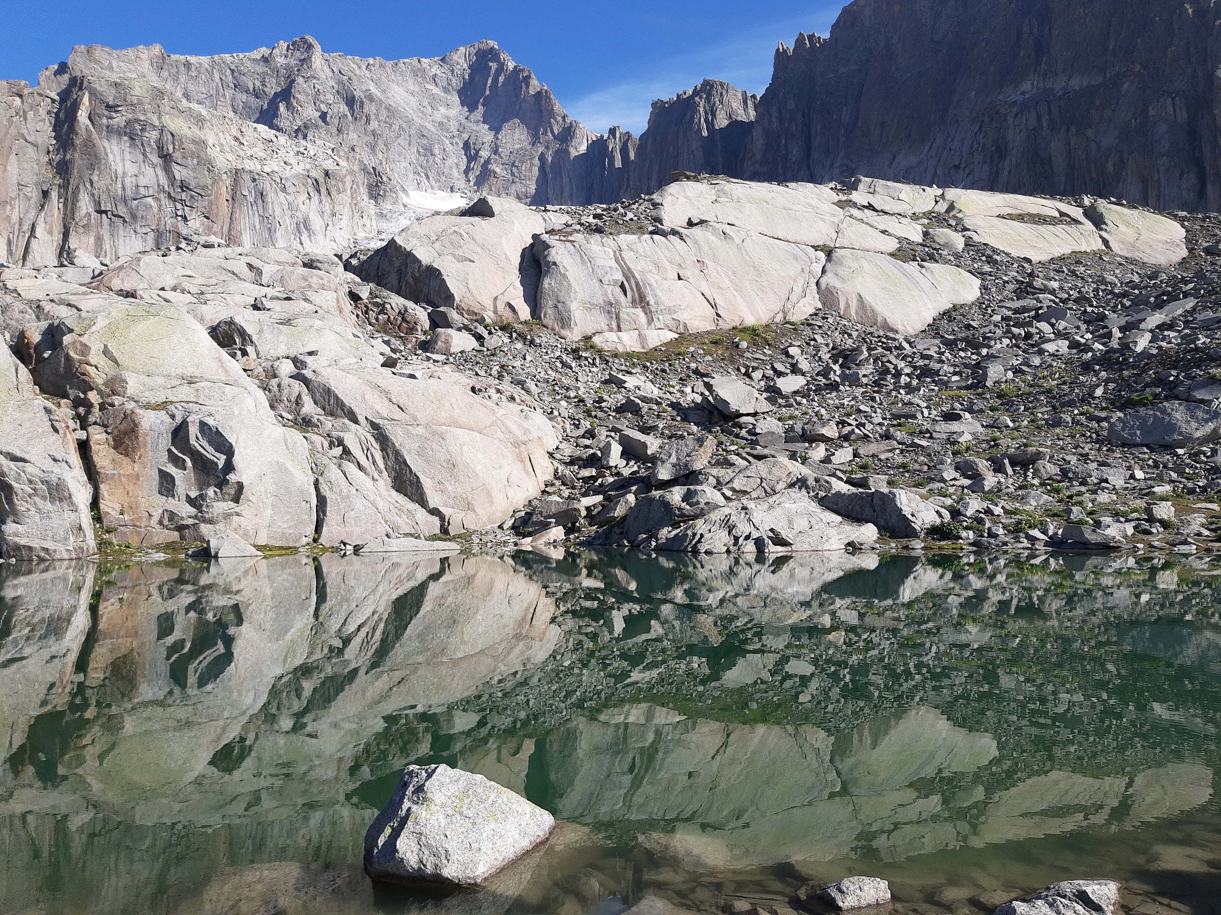 Aar granite slabs and spires reflected in a clear tarn below the Sidelen hut, snow-free in high summer.