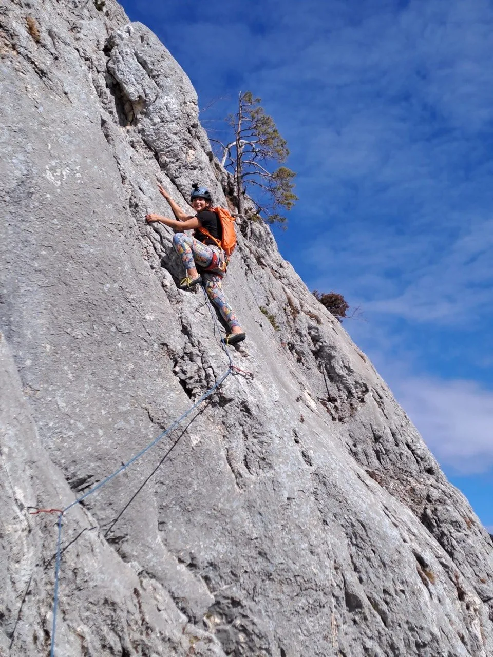 A climber traverses the steep grey rock face of the Eulengrat ridge against a blue sky.