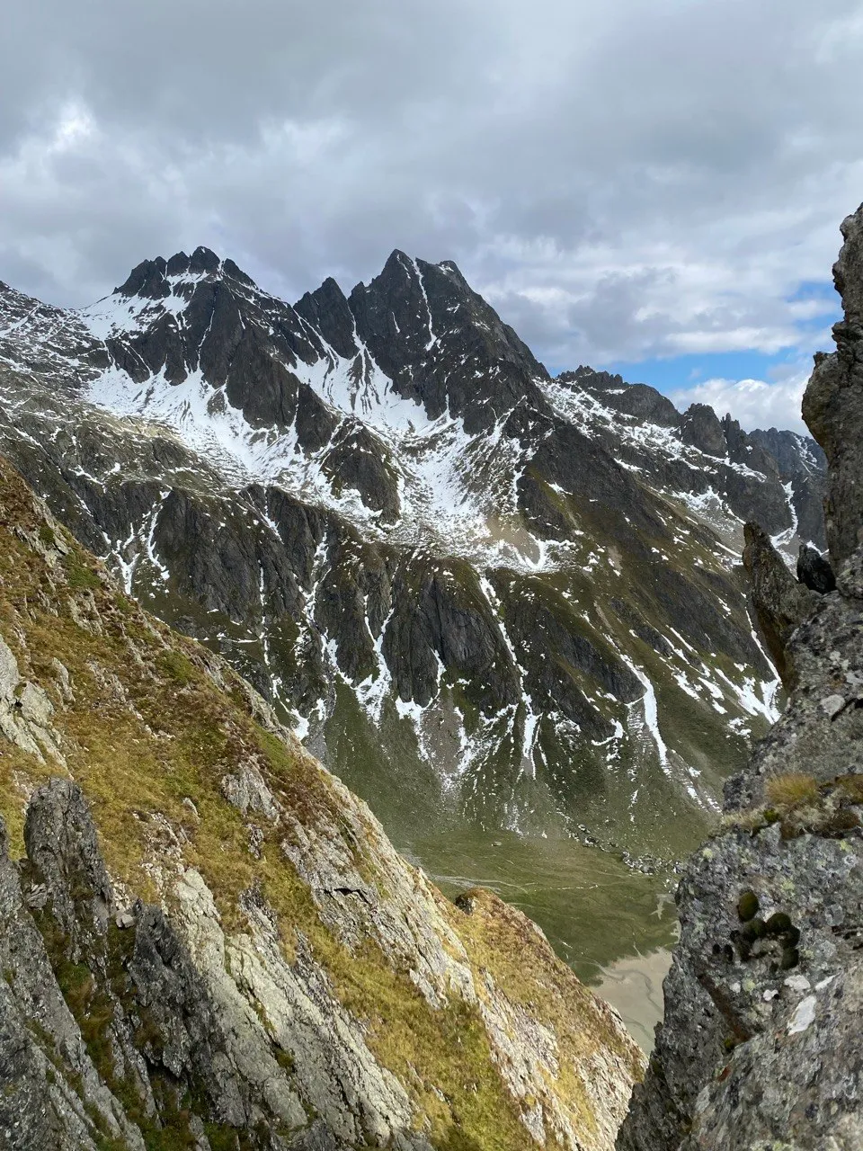 Snow-streaked peaks framed by rock, with a green valley floor visible below.