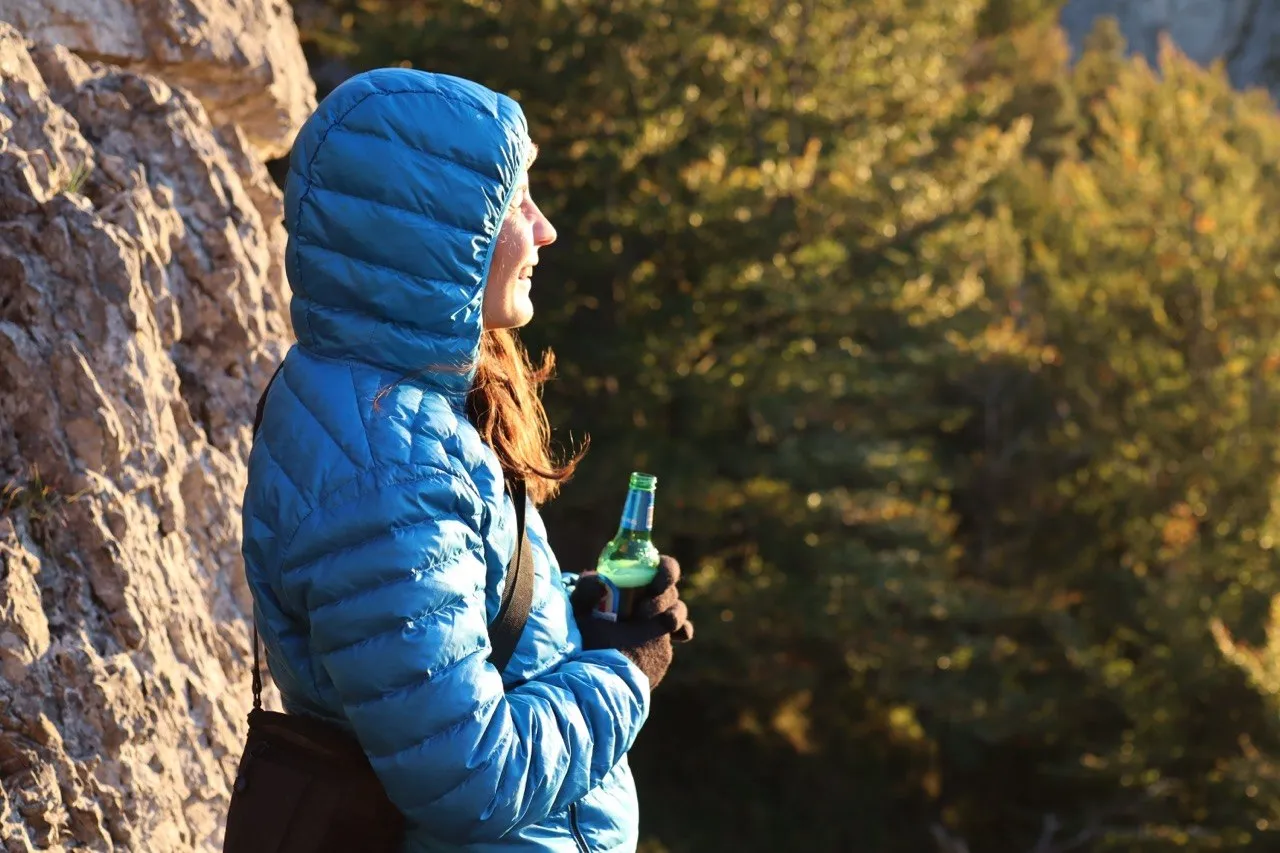Portrait of a hiker in a blue hooded jacket, pausing on the trail with a drink in hand.
