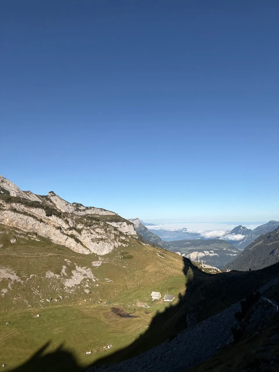 Looking down onto two alp huts in a green hollow, a sea of cloud over the valley beyond.