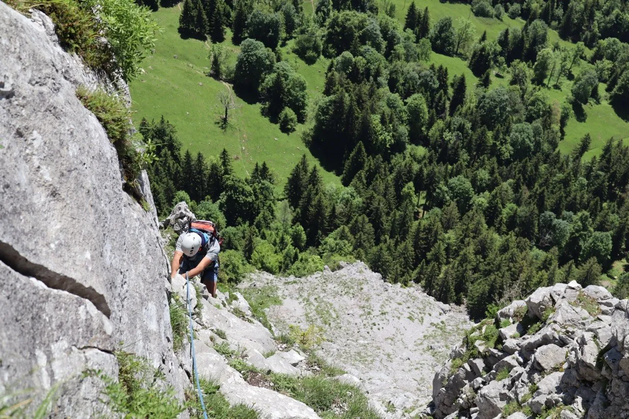 Helmeted climber on a rocky ridge with dense forest far below.