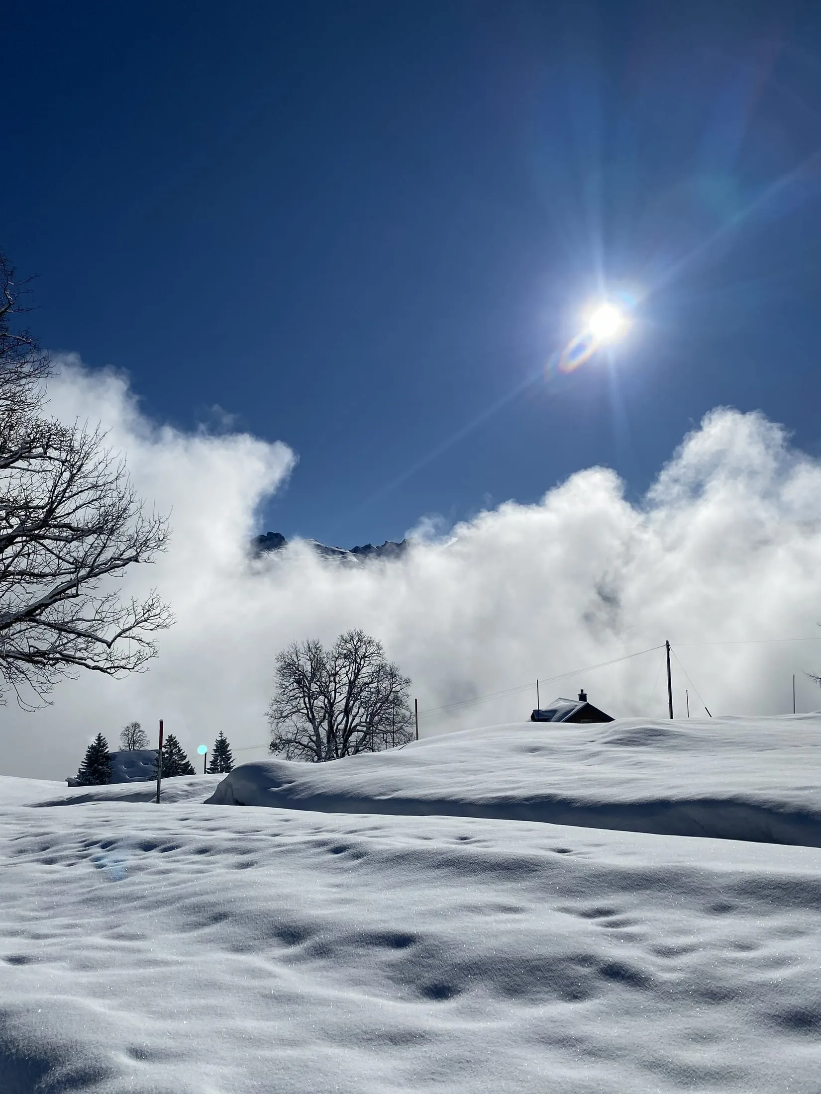 Clouds breaking up over a small cabin on a deeply snowed-in slope.