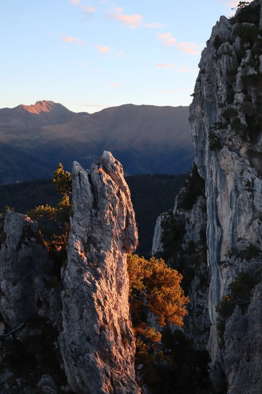 A slender rock pinnacle rising against layered mountain ridges at golden hour.