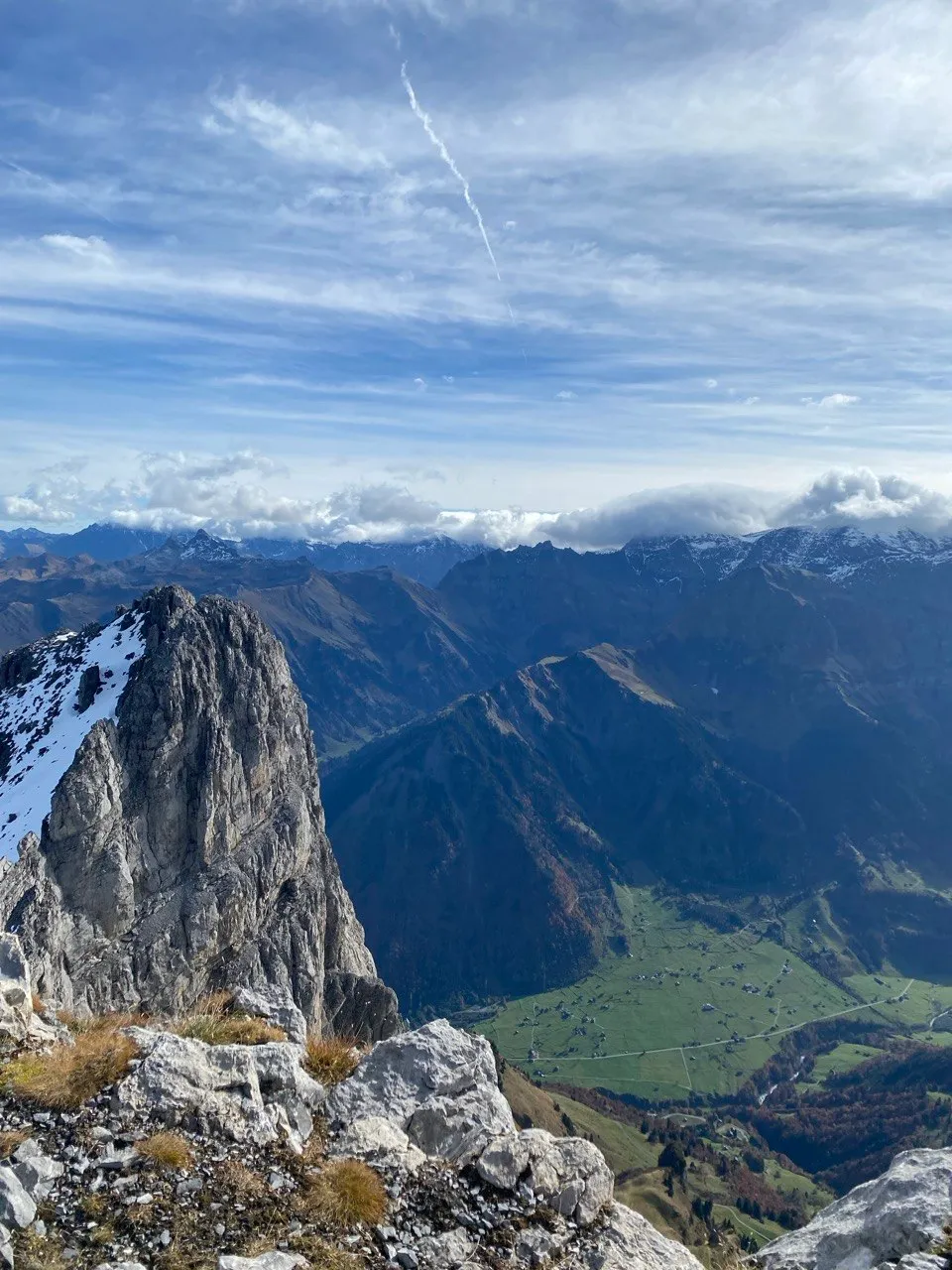 Jagged rocky summit with patches of snow above a green alpine valley.