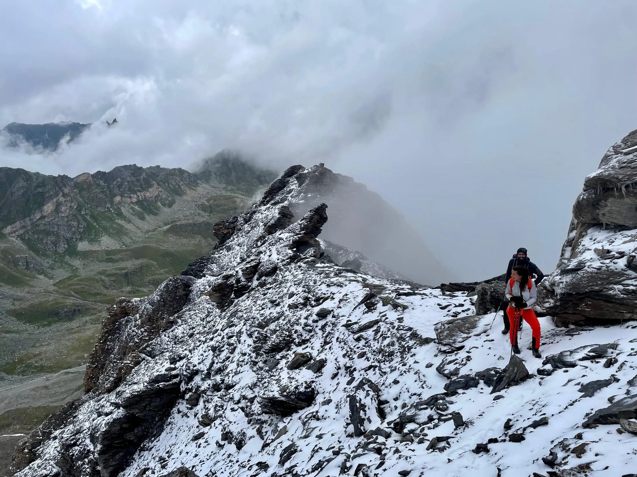 A person on the snowy ridge in cloud-covered terrain.