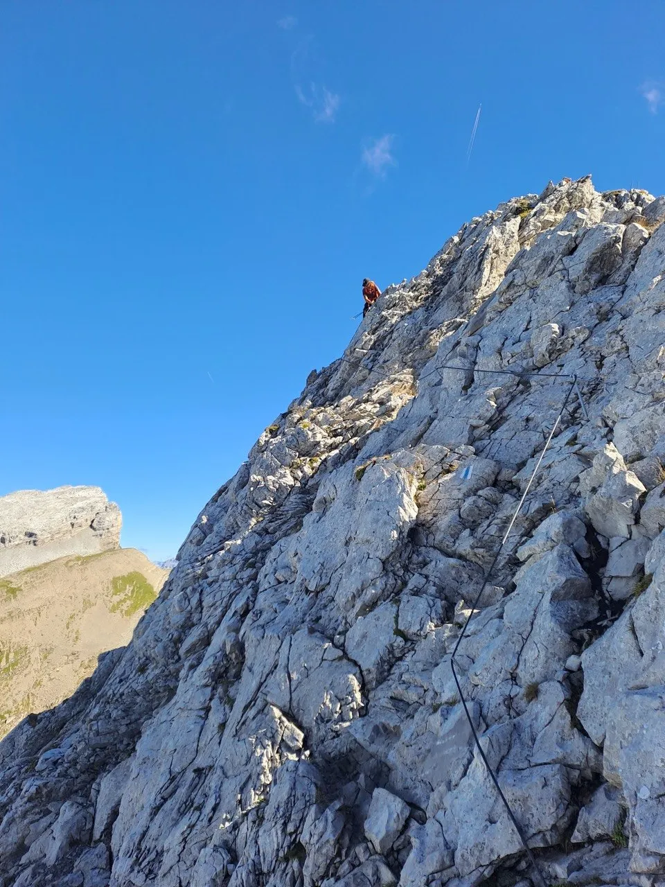 Scrambling section on pale limestone: a small figure high on the ridge, a chain running up the rock.