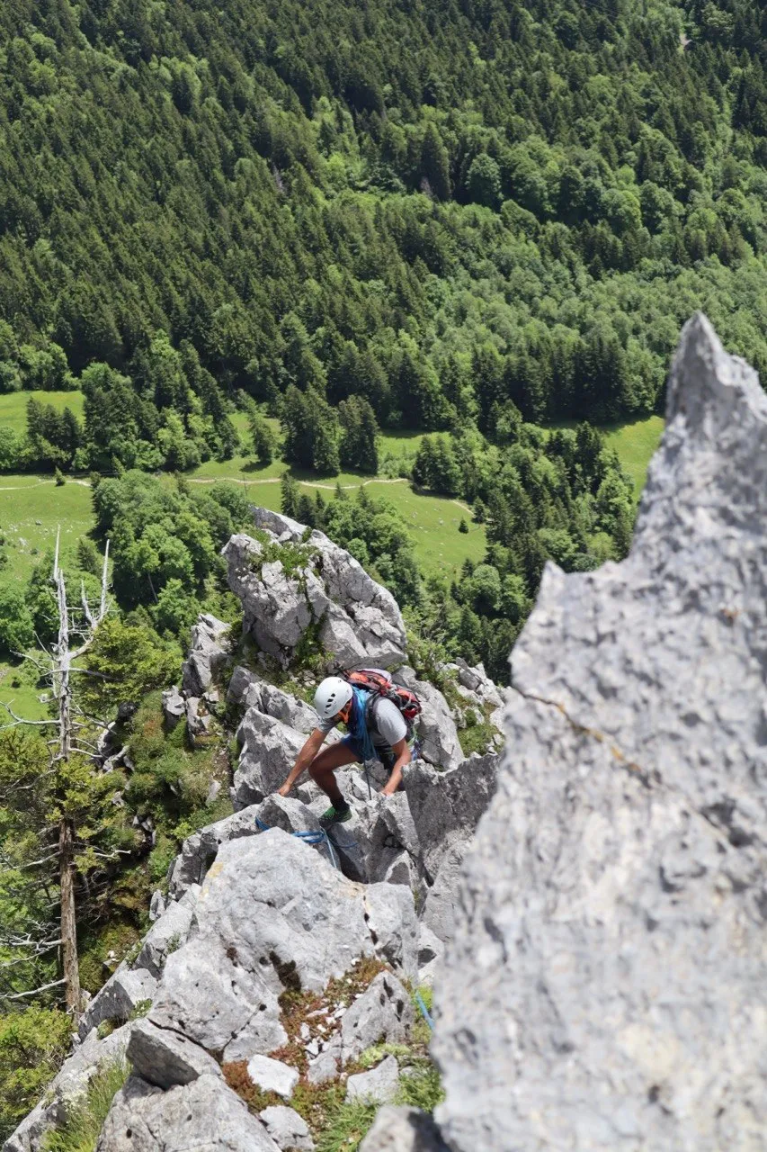 Climber scrambling up a rocky ridge beside a pointed limestone spire.