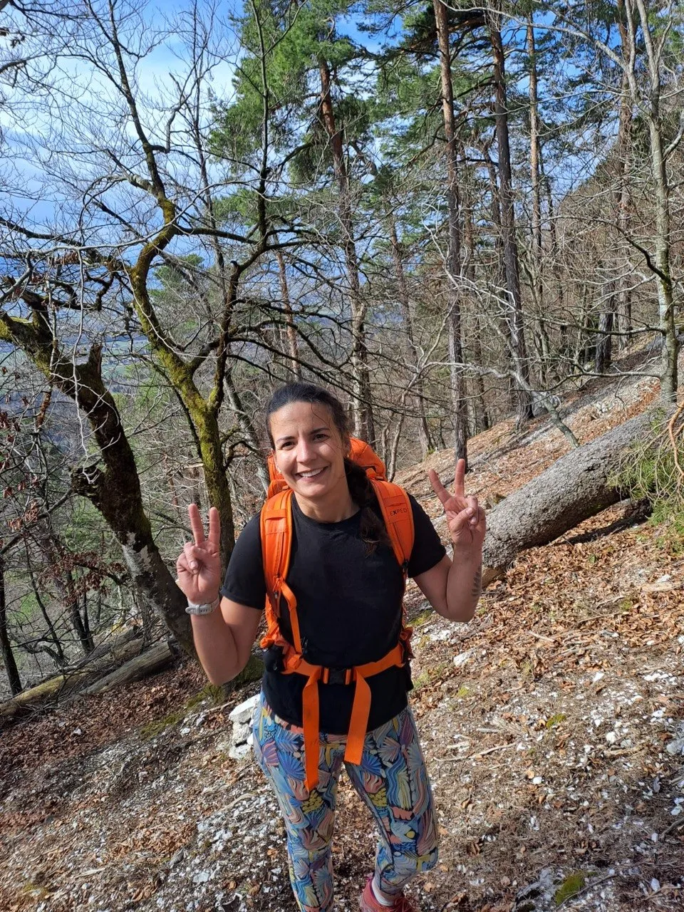 A hiker with an orange backpack flashes a peace sign in the forest after the climb.