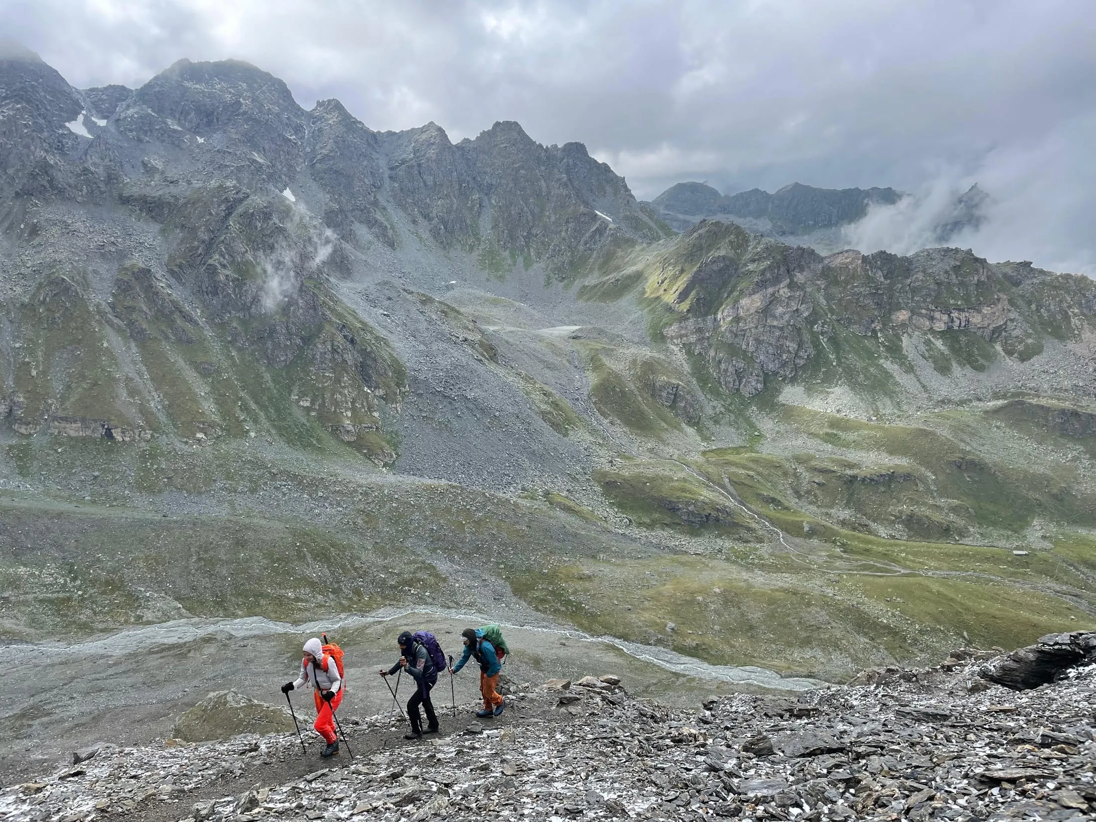 A group ascending a long scree slope under clouds.
