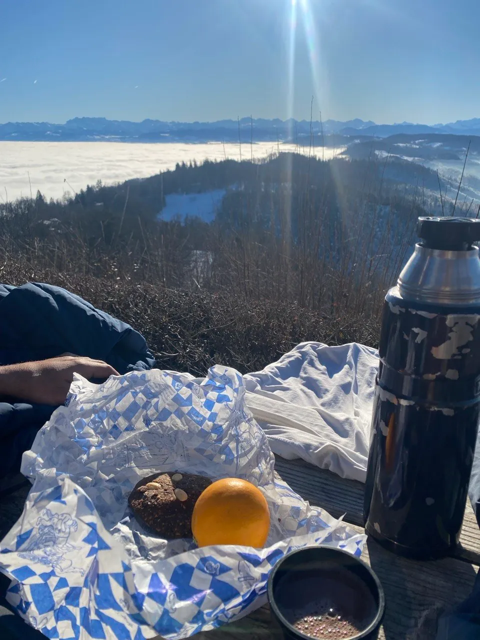 Picnic with an orange and tea above a sea of fog, Alps on the horizon.