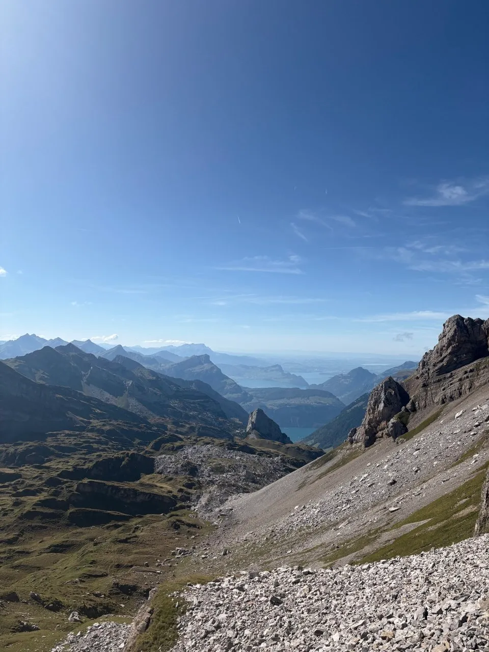 A wide view over scree slopes to peaks and the deep-set Urnersee under a blue sky.