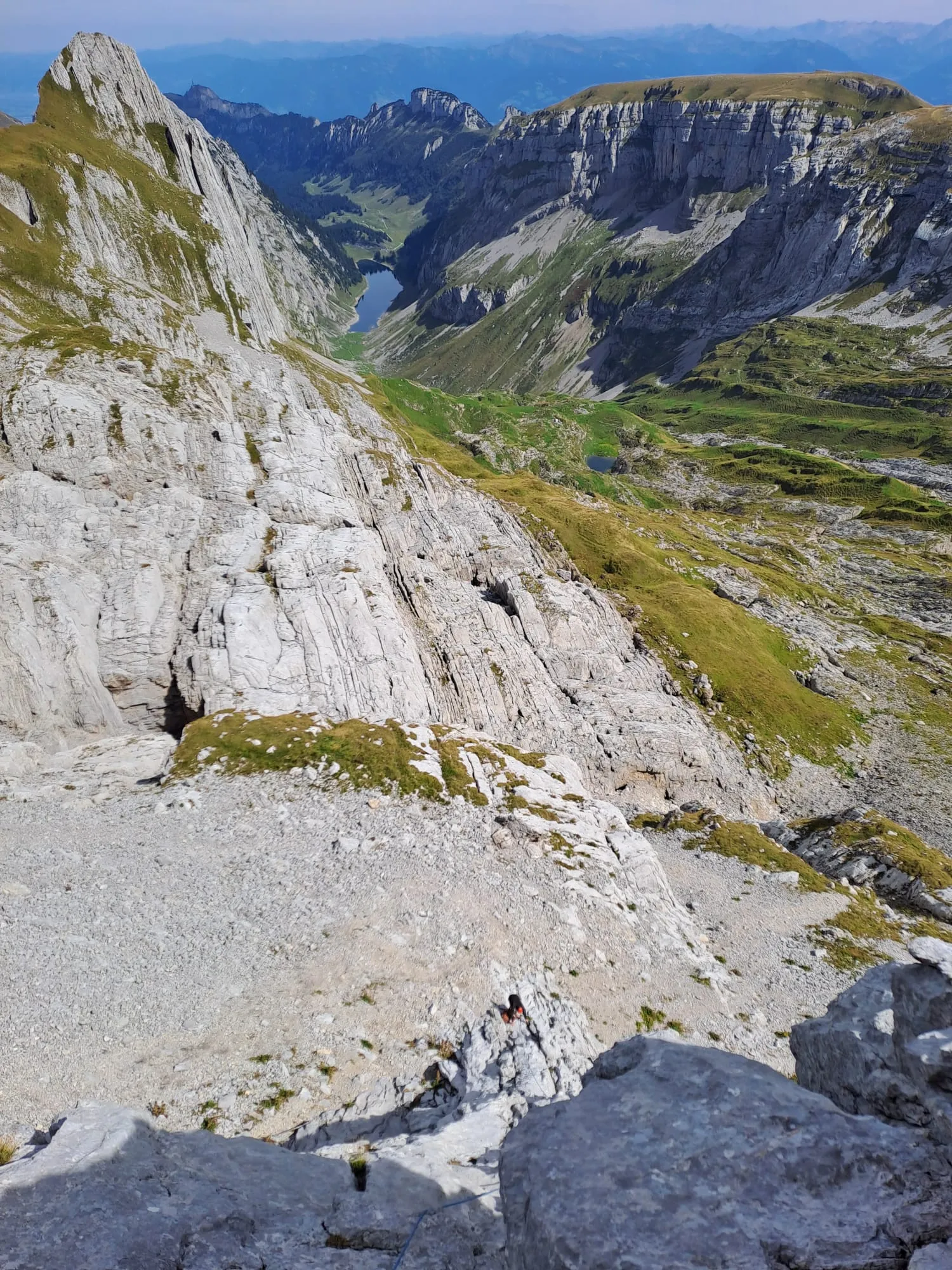 View down from the ridge to the Fälensee and the green Alpstein valleys, distant ranges layered in the haze.