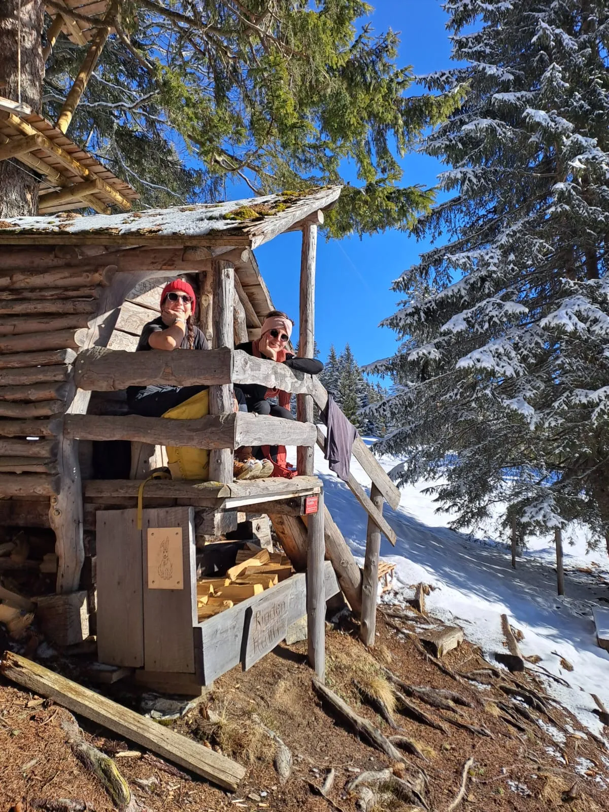 A break on the porch of a small wooden cabin beneath snowy firs.