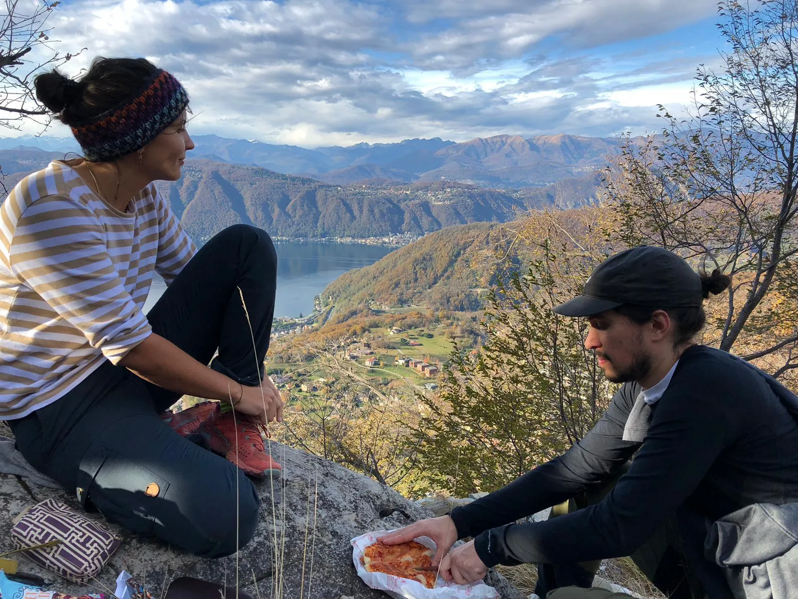 Two people sharing pizza on a rocky perch high above Lake Lugano.