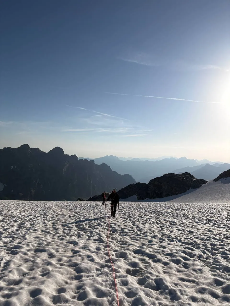 Two roped-up mountaineers crossing the glacier at dawn with the sun low on the horizon.