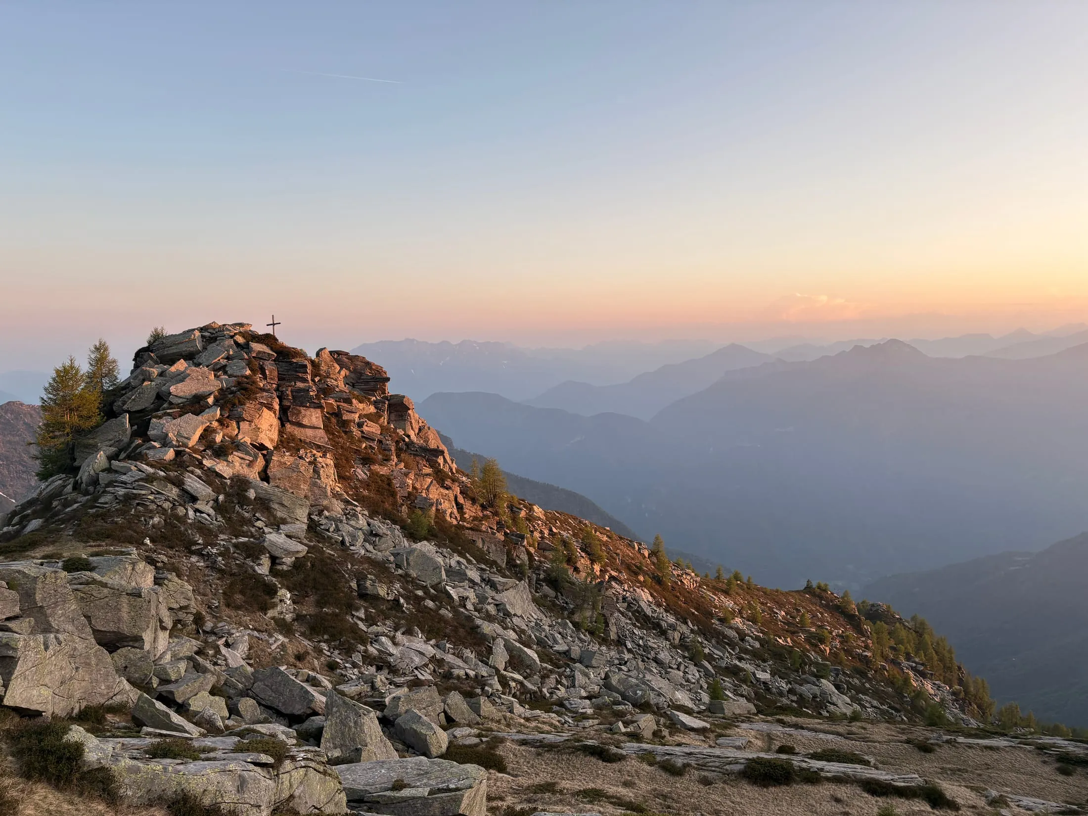 A rocky knoll topped with a small summit cross, glowing in warm dawn light.