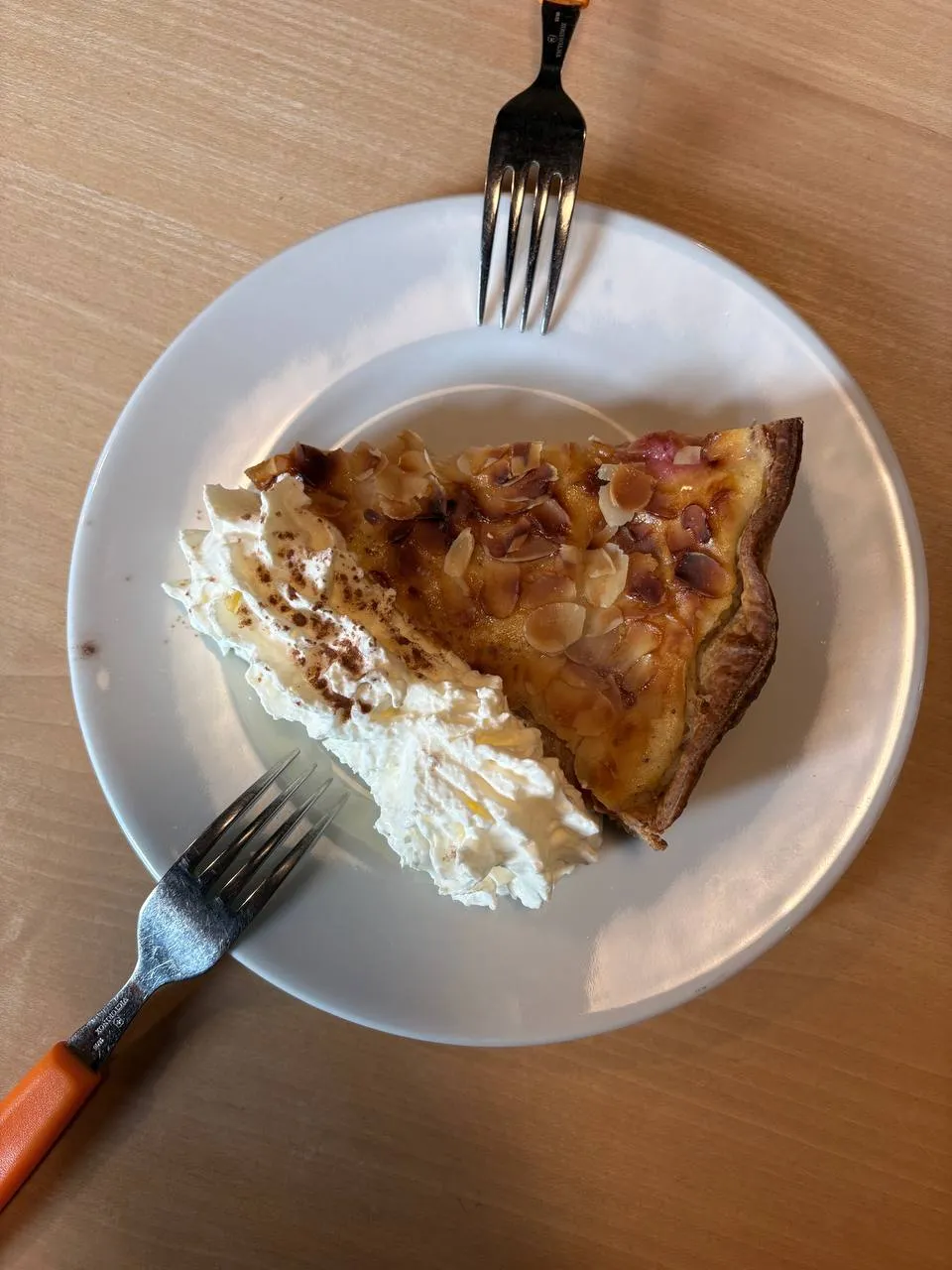 A slice of tart topped with toasted almonds and a dollop of cream on a plate at the hut, with two forks.