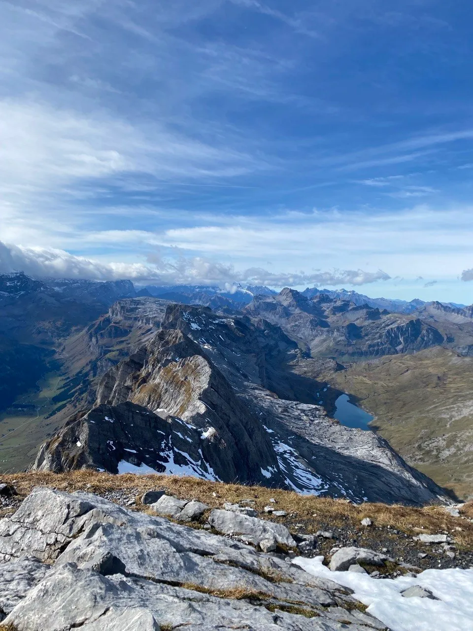 Snow-dusted ridge overlooking a mountain lake and the alpine chain.