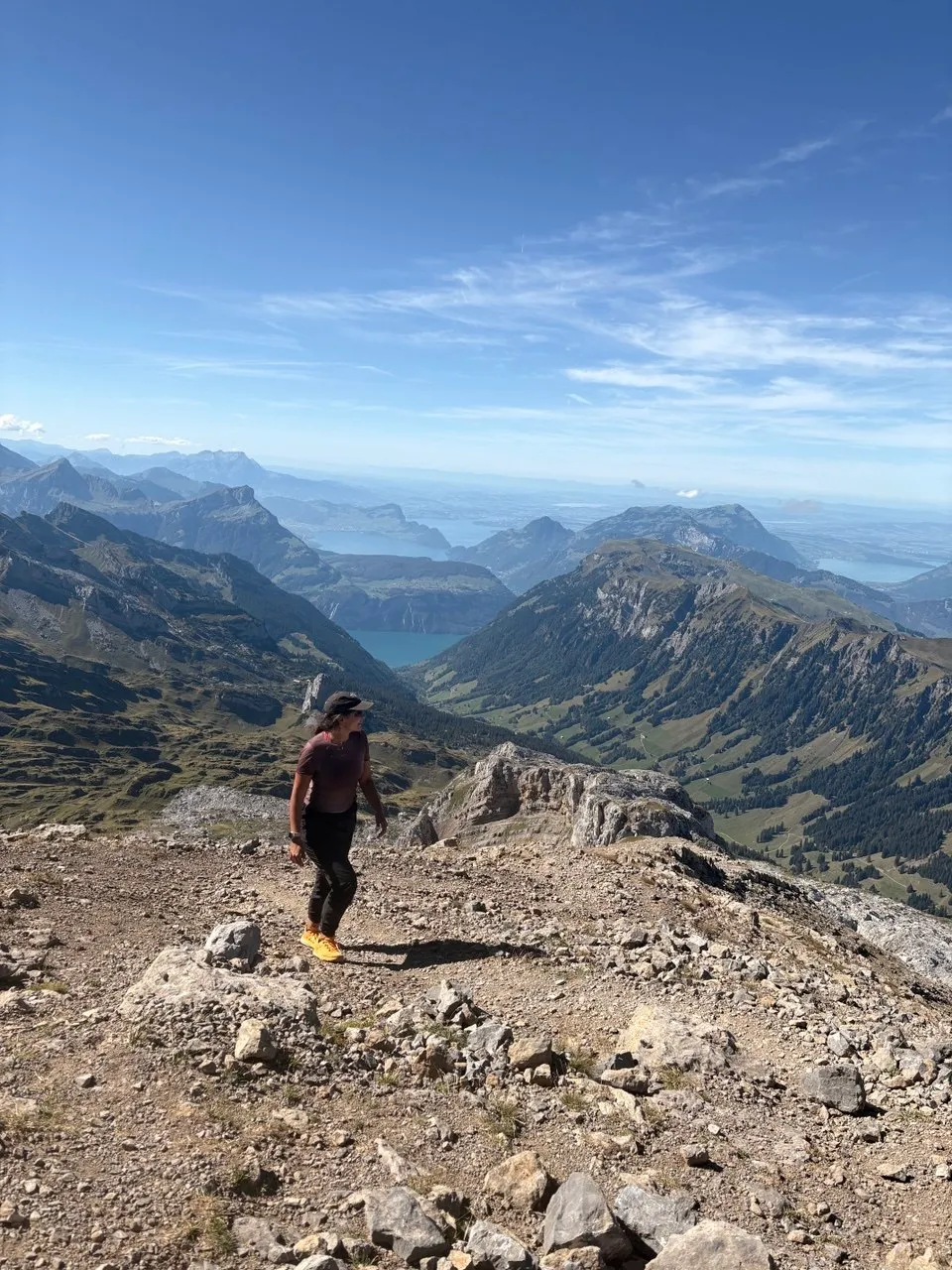 Hiker crosses a scree slope, with Lake Uri and Lake Lucerne far below between the ranges.