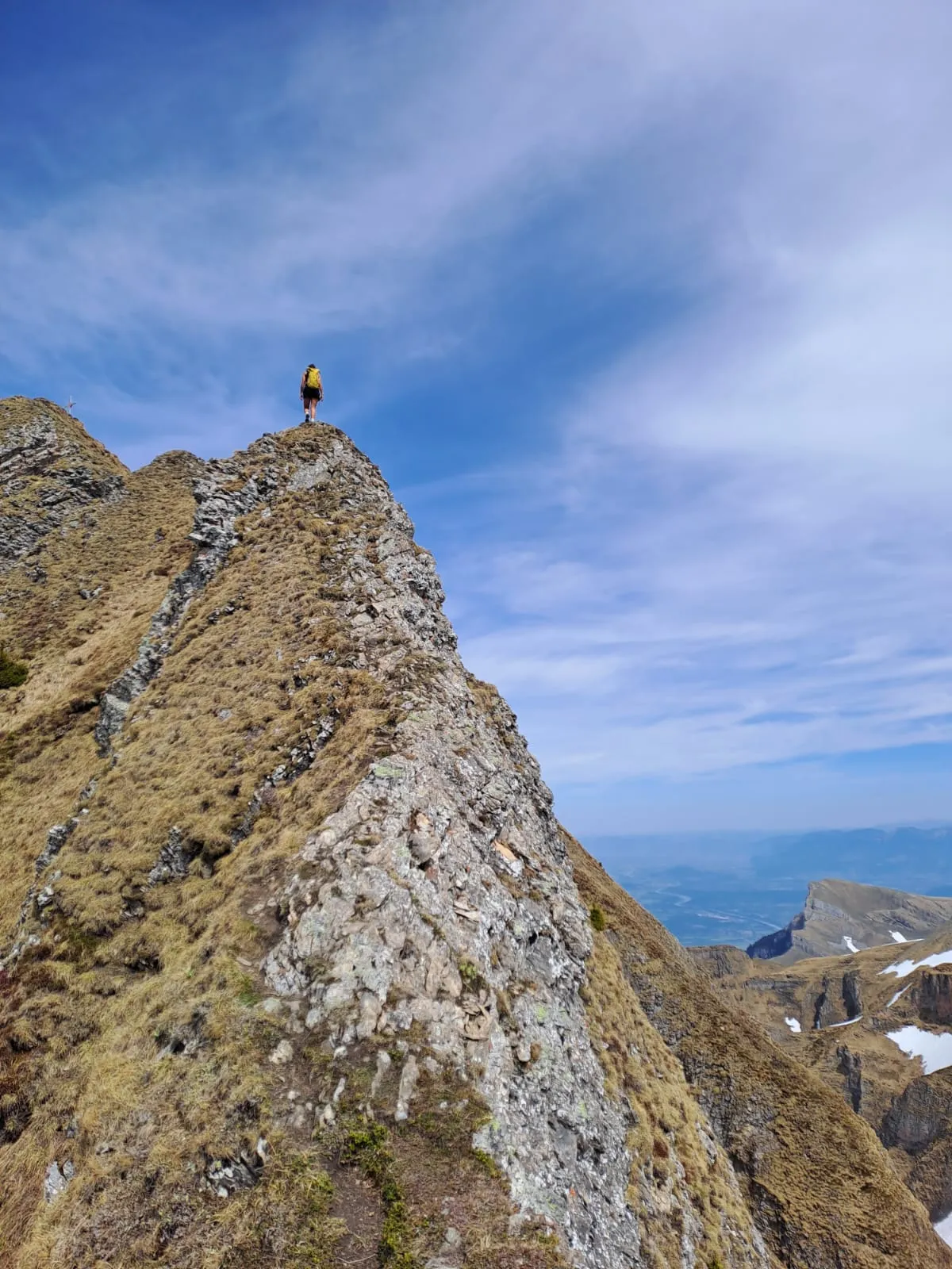 A small figure standing on the airy rocky pinnacle of the summit ridge.