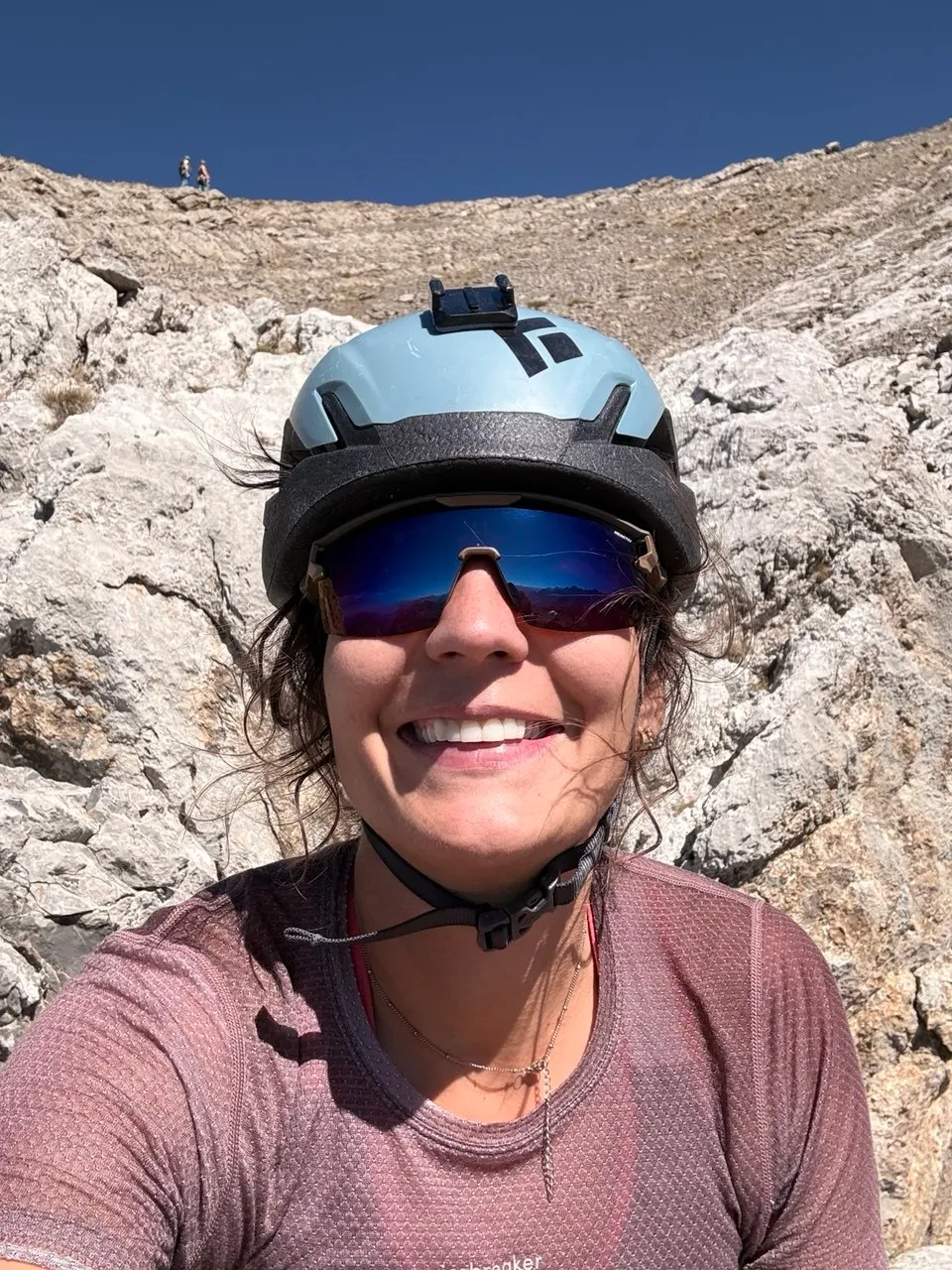 Selfie of a smiling woman in a climbing helmet and sunglasses against pale limestone rock.