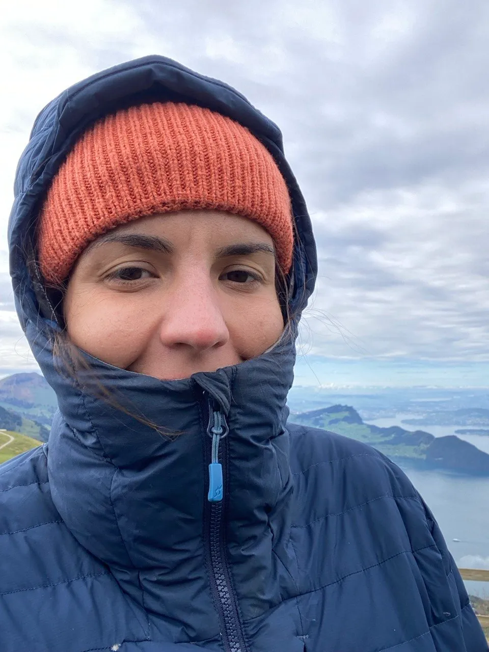 Portrait of a hiker in an orange beanie, lake in the background.