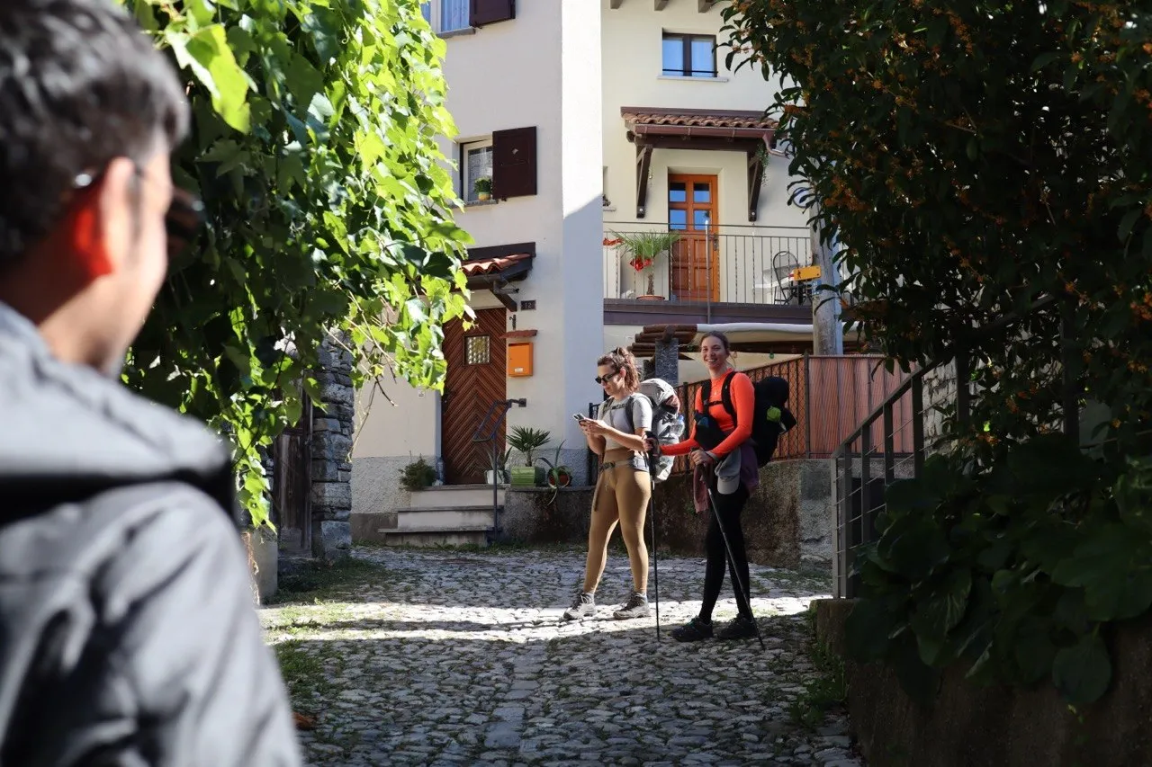 Two hikers with backpacks arriving in a quiet village alley to start the trail.