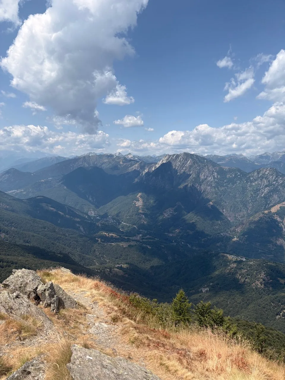 The stony trail on the ridge crest, looking out over a deep forested valley to a long line of jagged peaks.