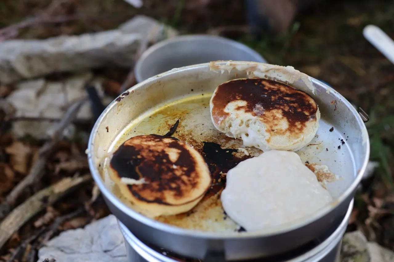 Pancakes cooking in a camping pot over a trail stove.