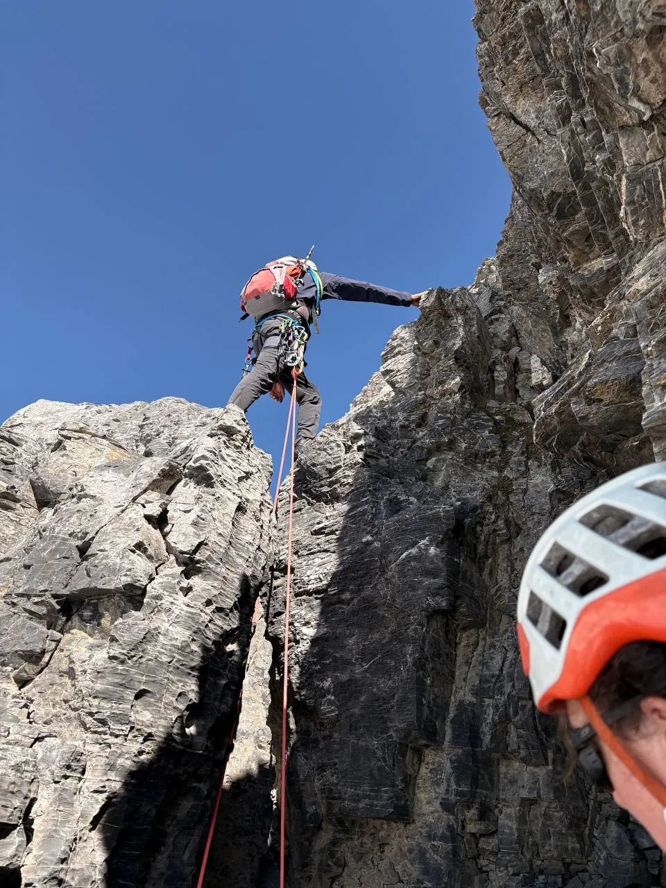 A climber high-stepping over loose rock on the fixed ropes below the summit.