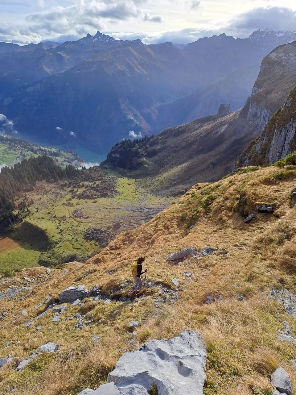 Hiker descending a grassy slope with a valley view ahead.