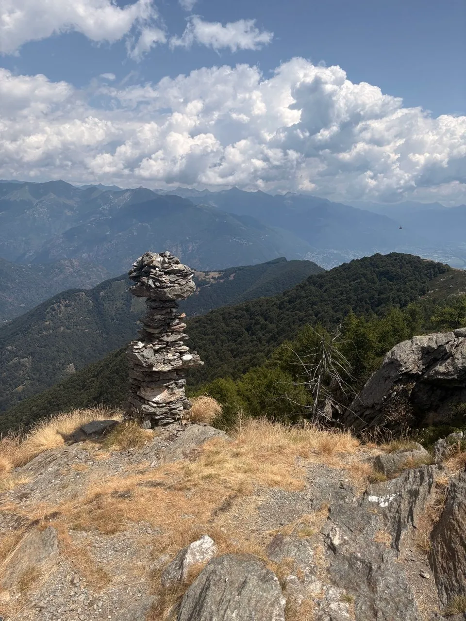 A tall stacked stone cairn standing on the rocky ridge, layers of hazy blue mountains behind.