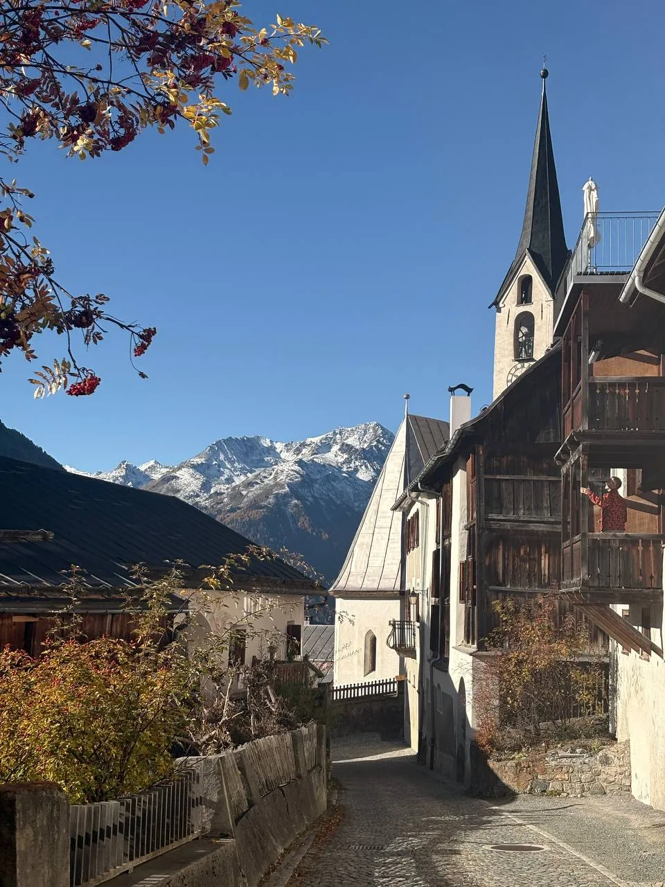 A narrow lane in Guarda with the church tower and carved wooden balconies, a snowy ridge on the horizon.