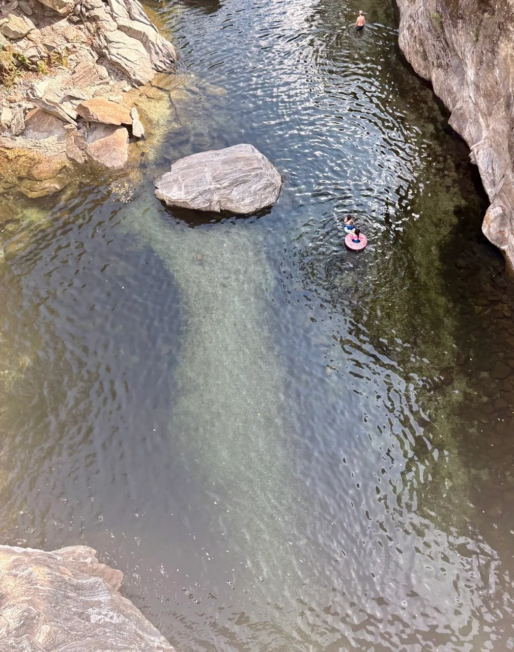 Looking down into a river gorge with clear green pools, a large pale boulder, and two people swimming.