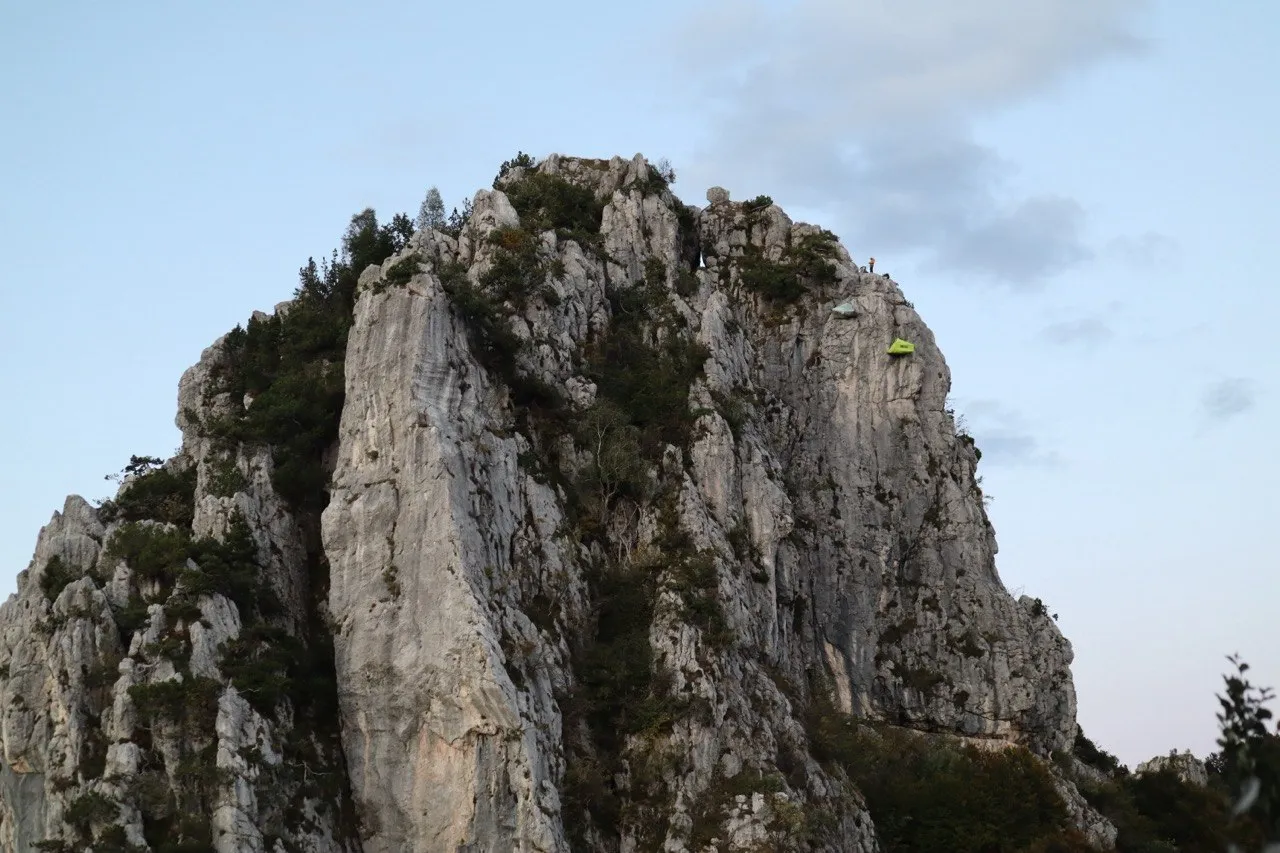 The jagged rock towers of Denti della Vecchia, with a hiker and tent visible near the summit.