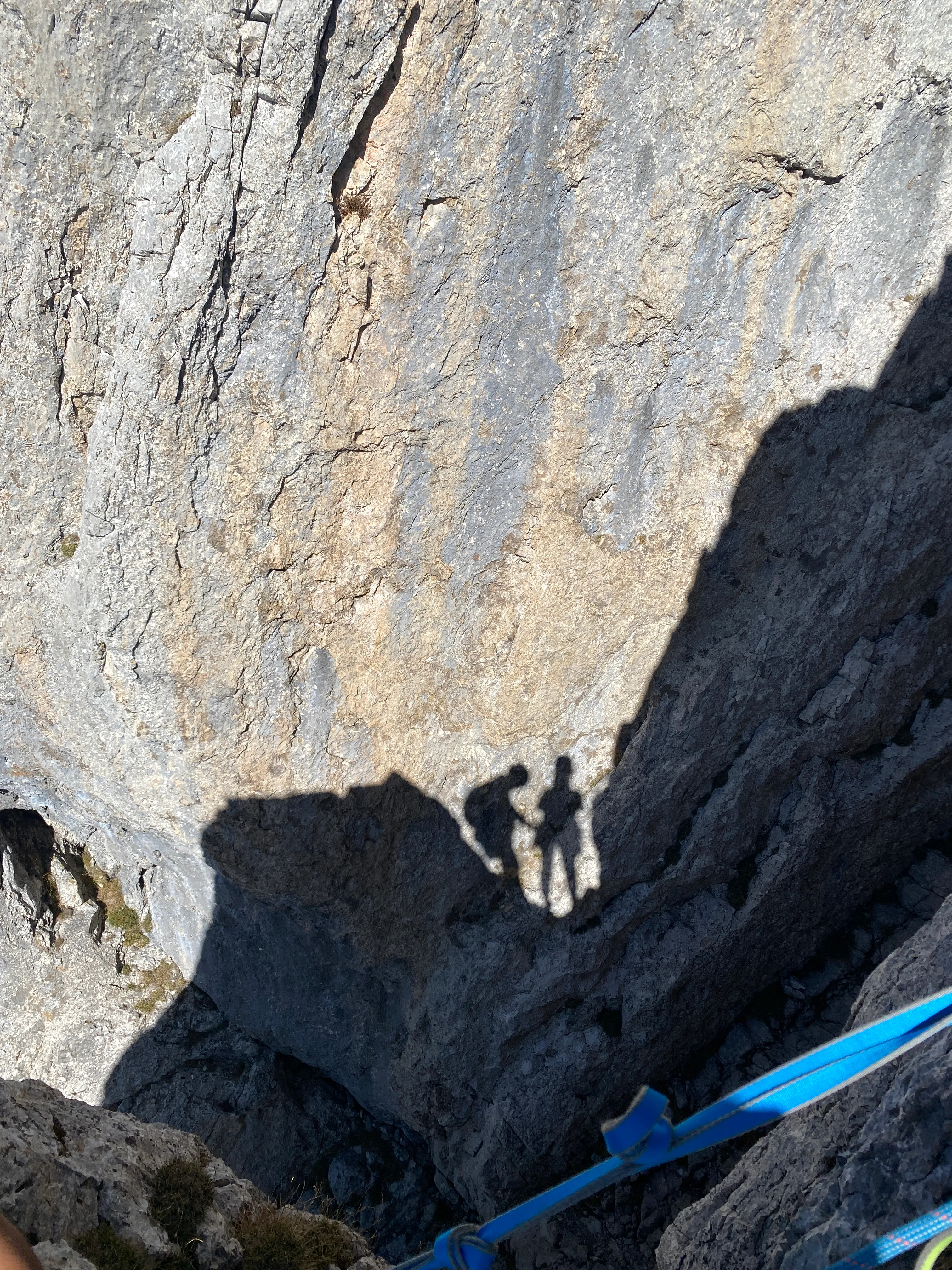 The shadows of two climbers cast on a sunlit limestone wall, a blue sling in the corner.
