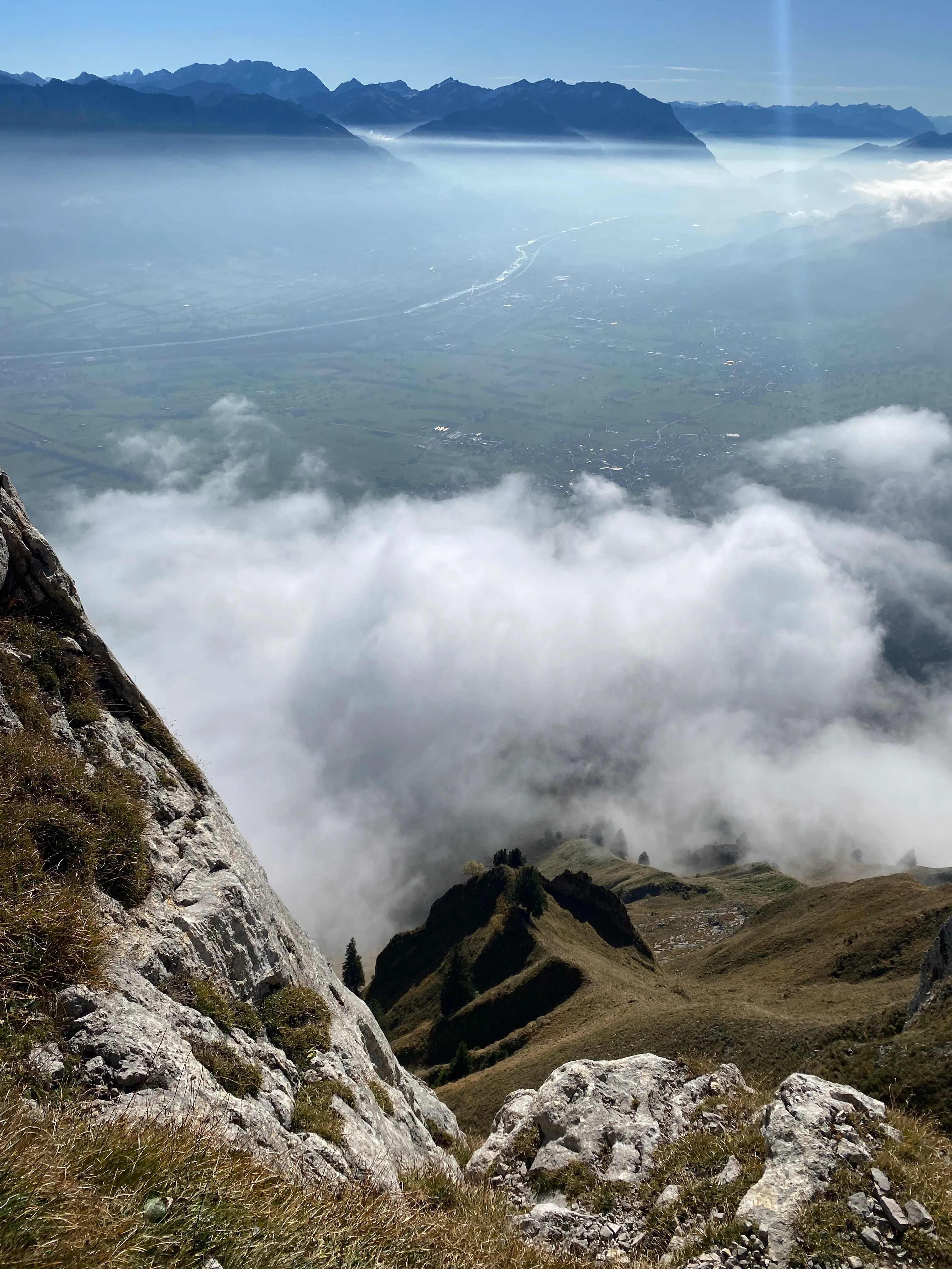 A view from high up over the Rhine valley, banks of fog below and distant alps on the horizon.