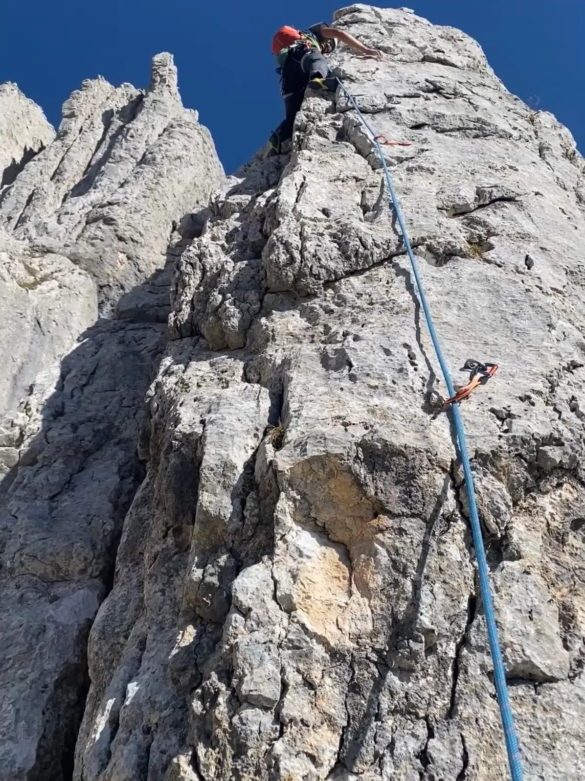 A climber in a red helmet pulling over the top of a rock tower, a blue rope running alongside.