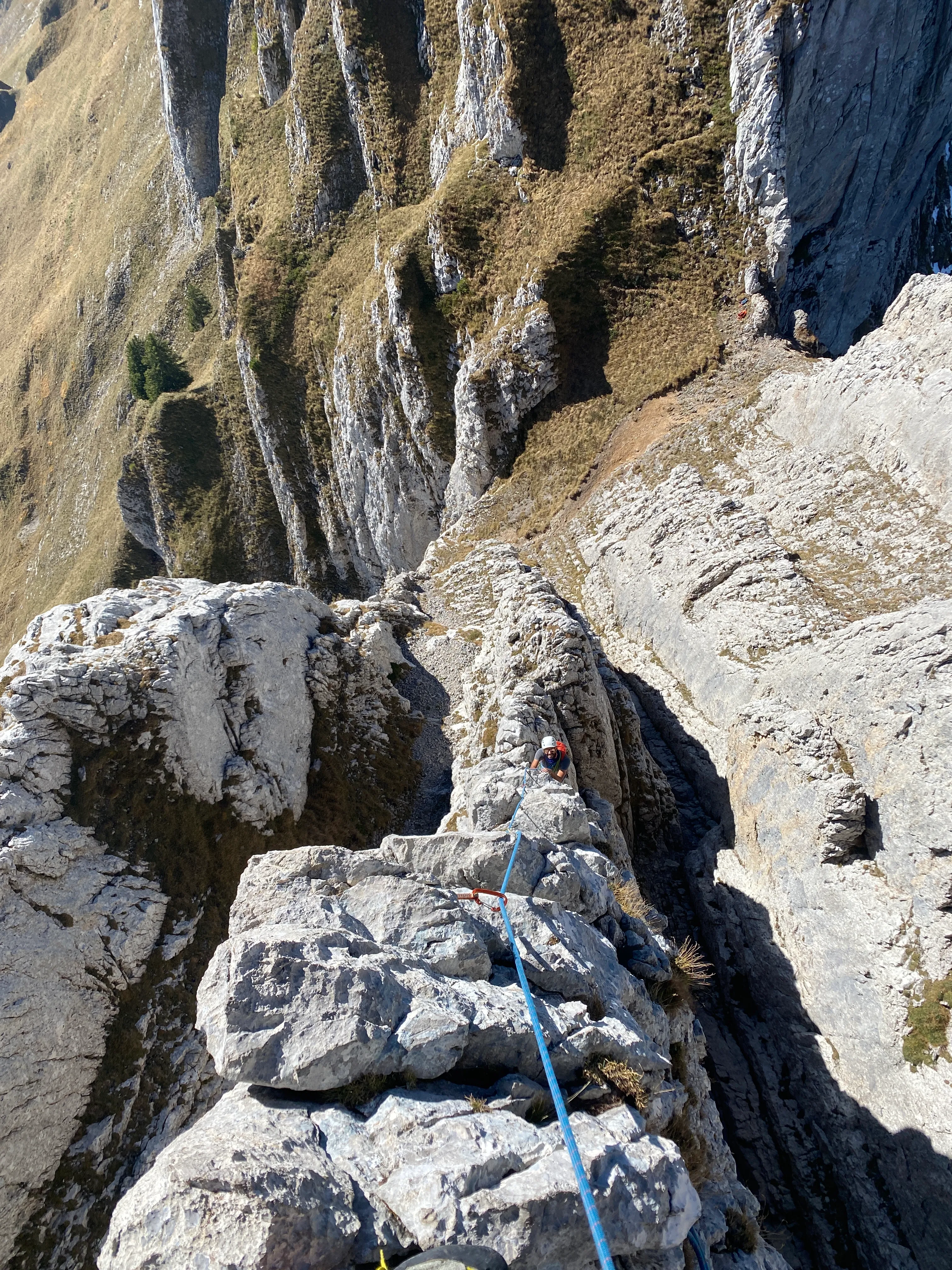 Looking back down the narrow ridge, a second climber coming up on the rope, the valley far below.