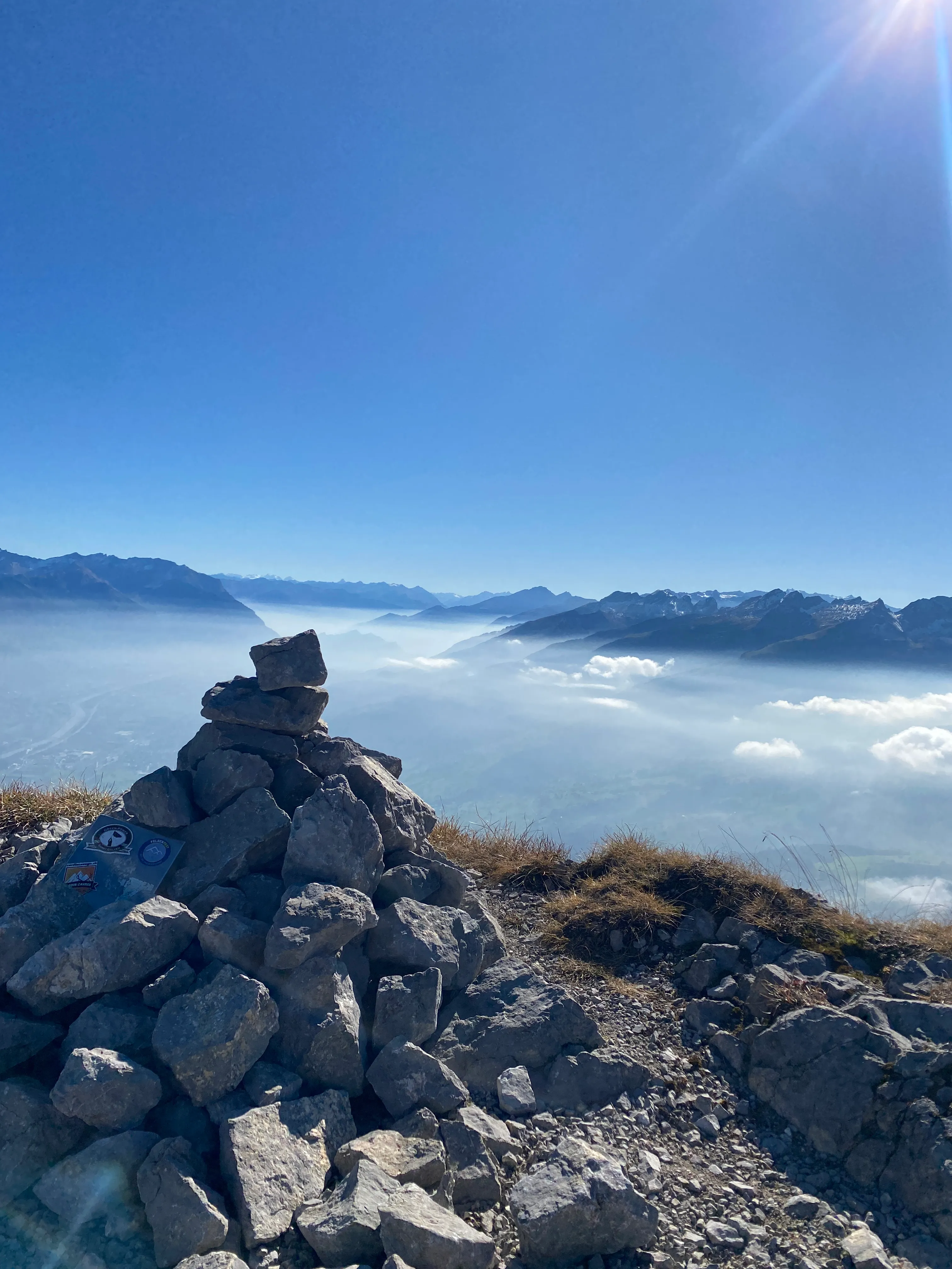 A summit cairn above a sea of fog, distant ranges hazy on the horizon.