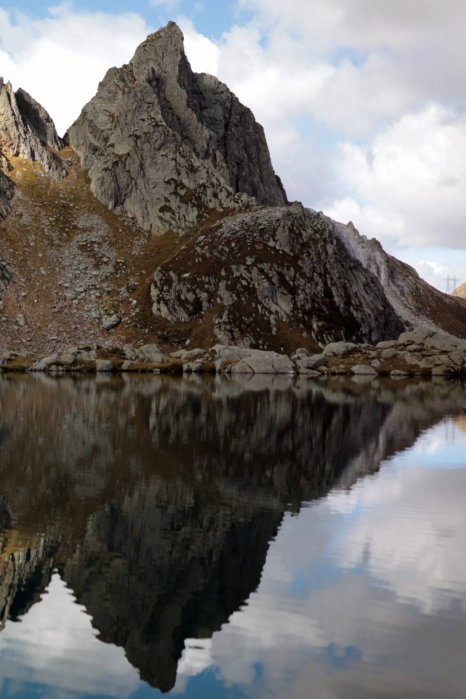 Sharp rocky spire mirrored in a perfectly still alpine lake.