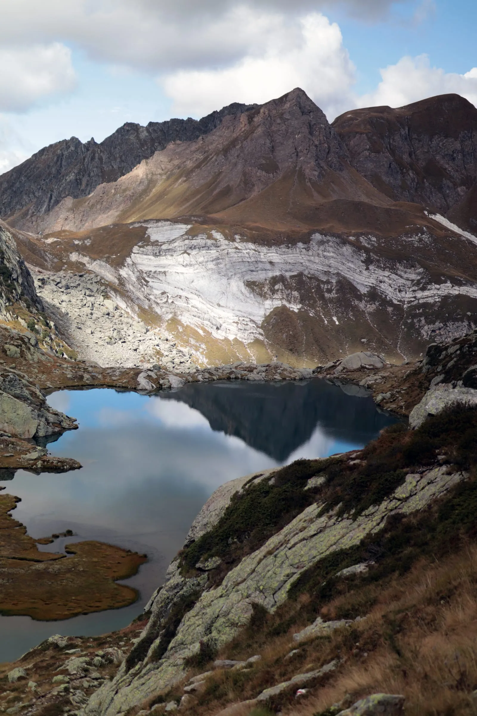 Turquoise alpine lake below rust-coloured slopes with leftover snow and jagged ridges.