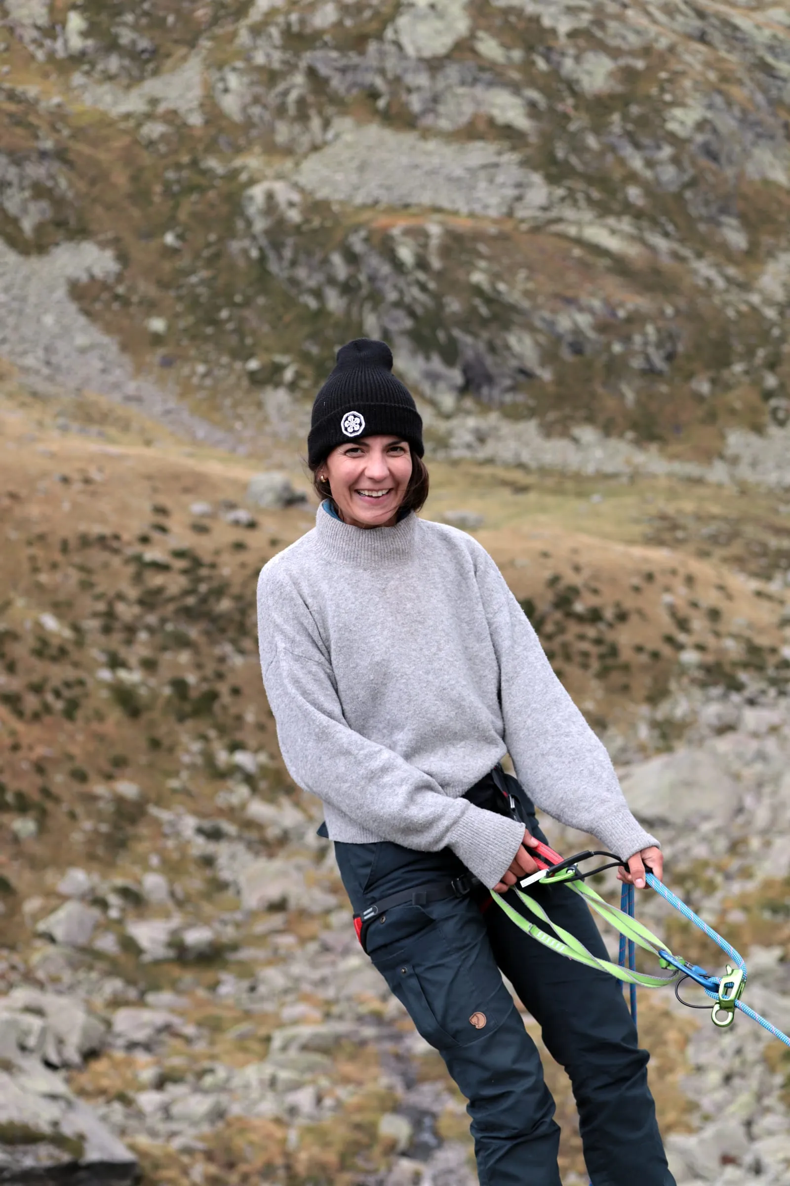 Cornelia in a beanie and harness laughing at the camera, carabiners and ropes in hand.