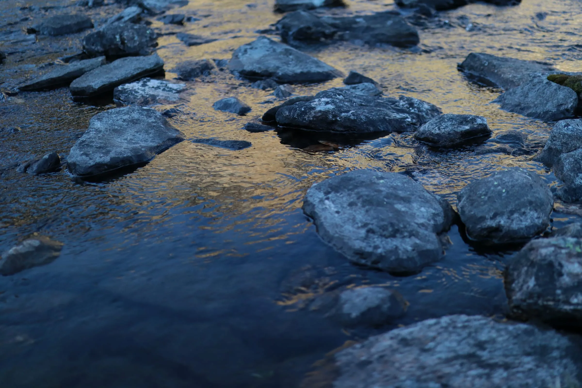 Rounded stones in shallow water with golden evening light glowing between them.