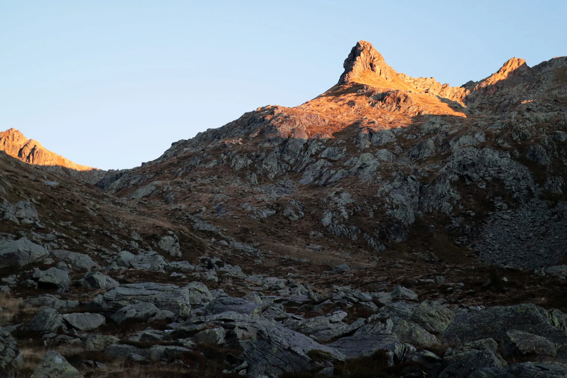 Last warm evening light on a rocky summit above a dark scree slope.