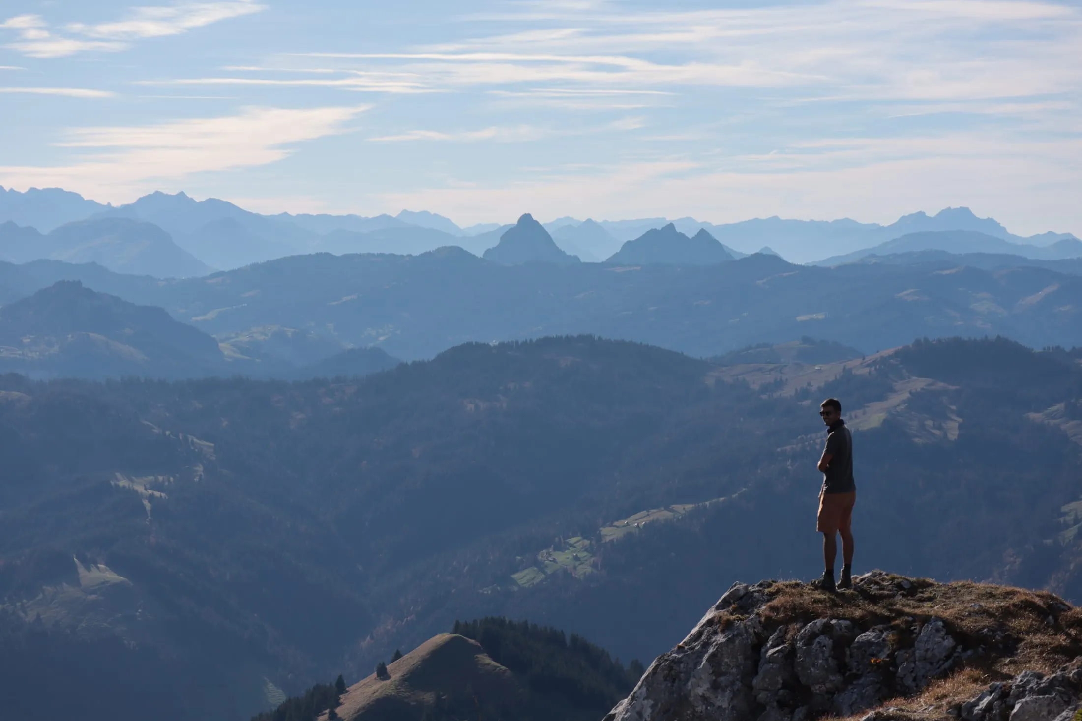 Excursionista sobre un saliente rocoso contemplando crestas prealpinas brumosas y escalonadas.